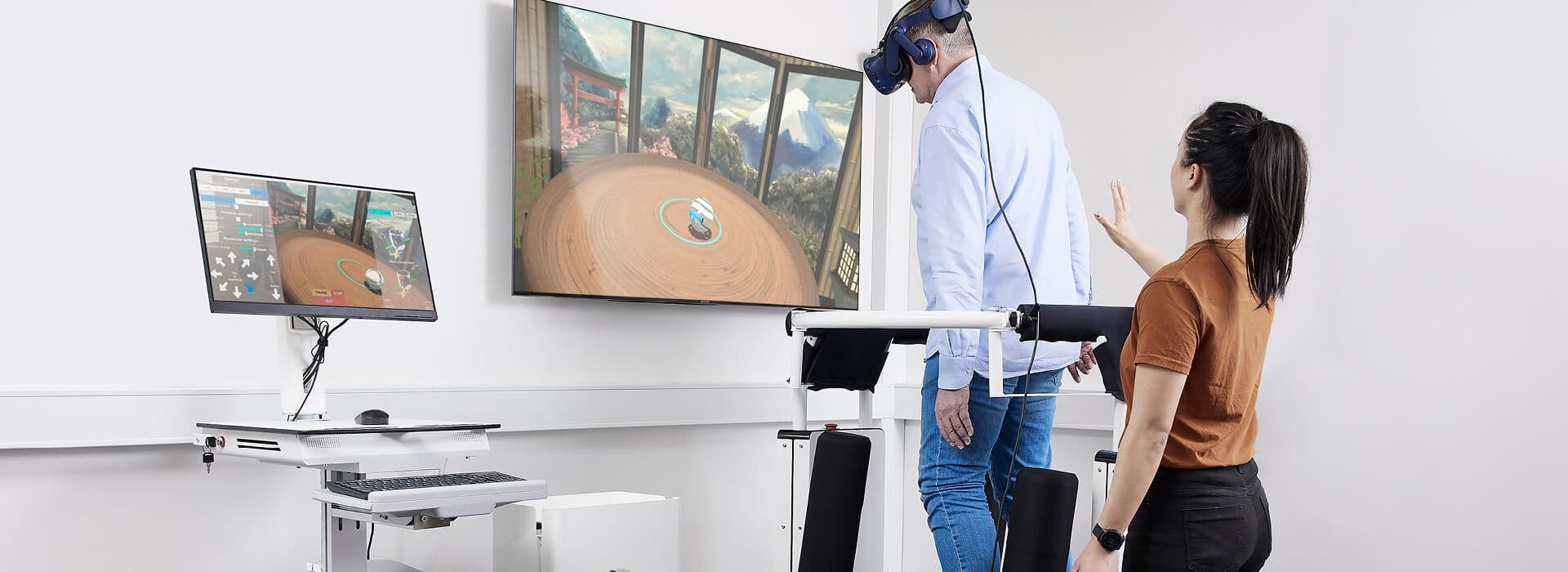 Audiolog hjælper en ældre mand med BalanceVR-udstyr i en balance- og rehabiliteringsøvelse på MotionVR-platformen.